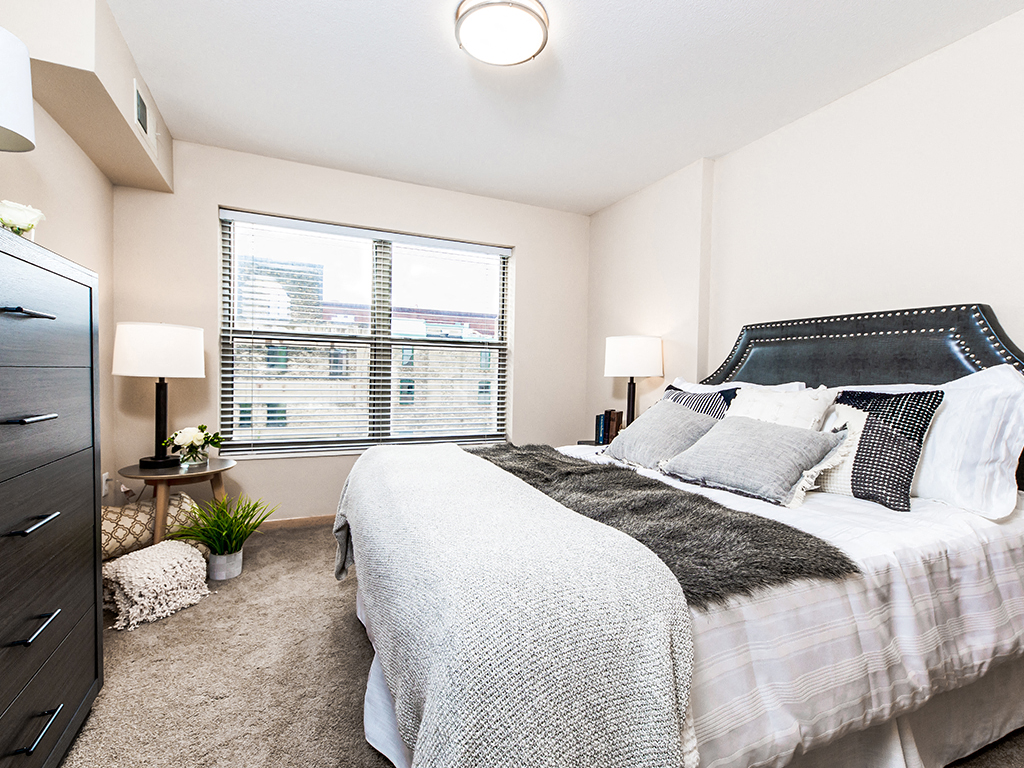 A bedroom with a large bed and a window with blinds.