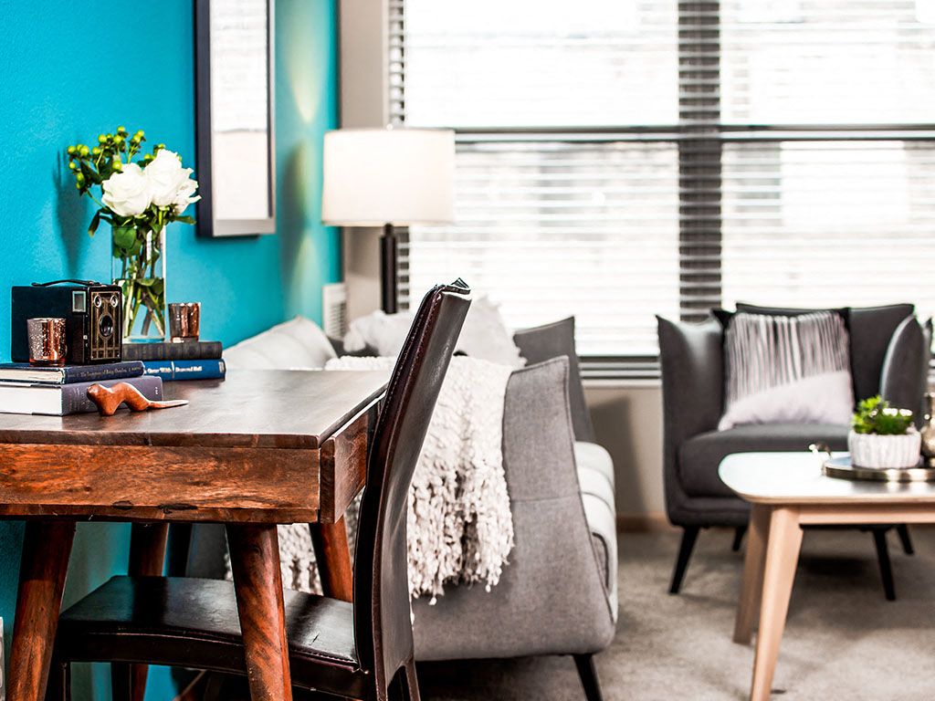 A living room with a blue wall and a wooden table with a vase of flowers and books.