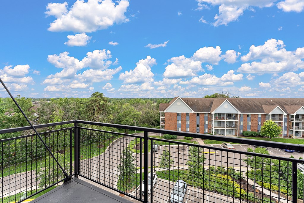 A balcony overlooks a green lawn and a brick building.
