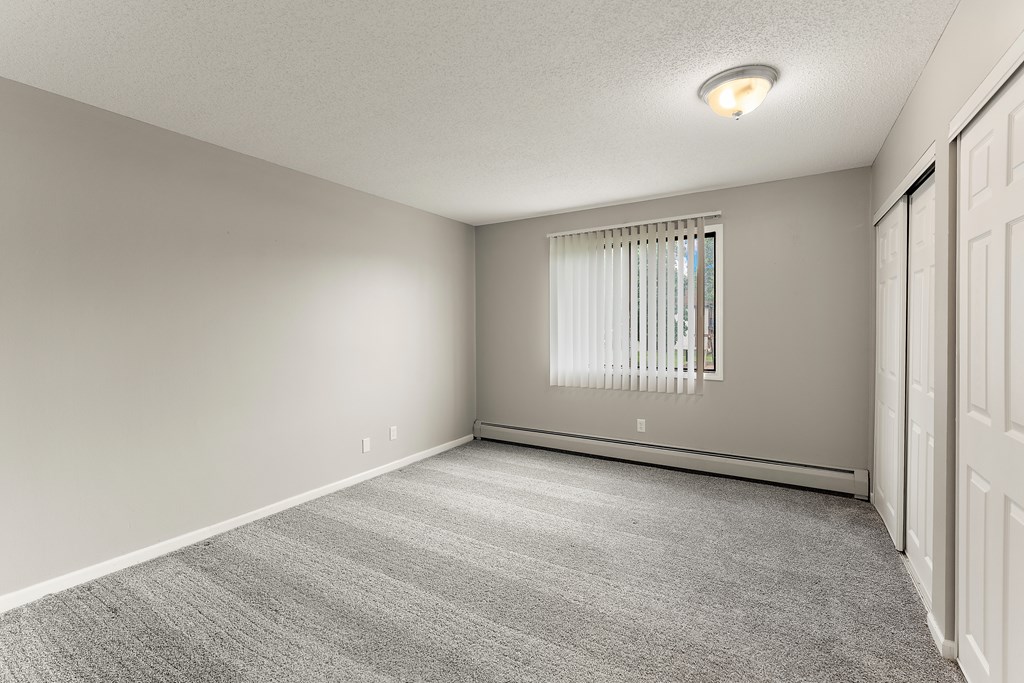A room with a carpeted floor and a window with blinds.