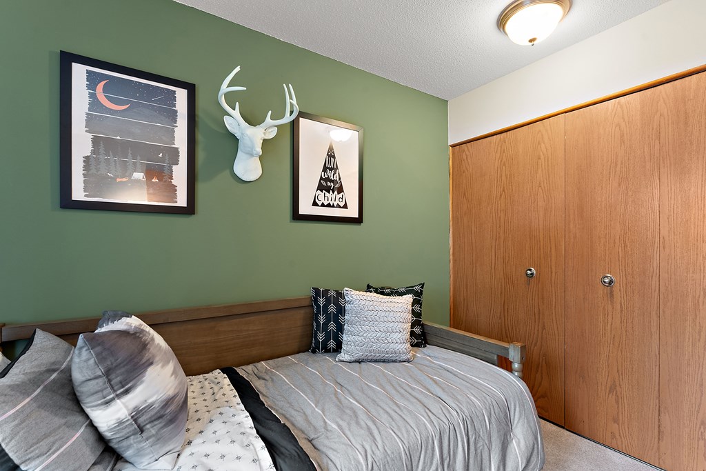 A bedroom with a bed, pillows, a deer head decoration, and a wooden wardrobe.