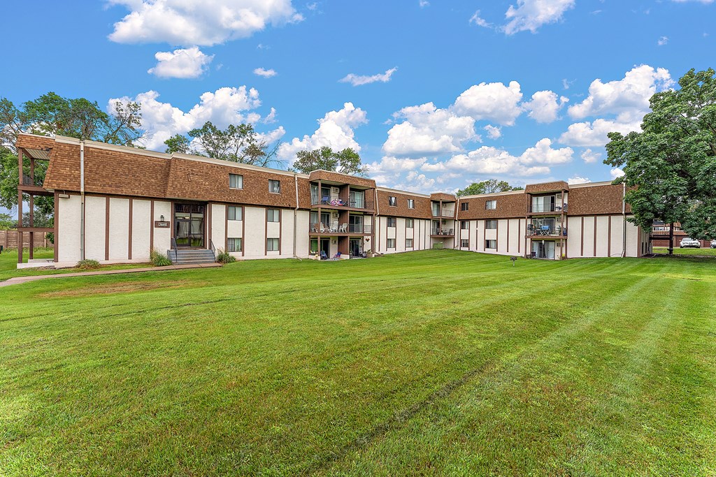 A large grassy field in front of a building with a blue sky and white clouds.