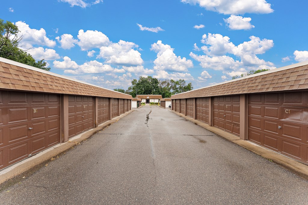 A long, narrow road flanked by brown garage doors under a blue sky with clouds.