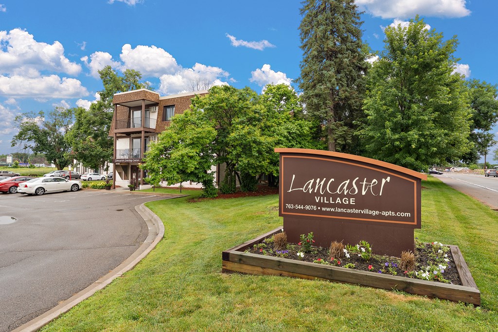 A sign for Lancaster Village is in the foreground of a grassy area.