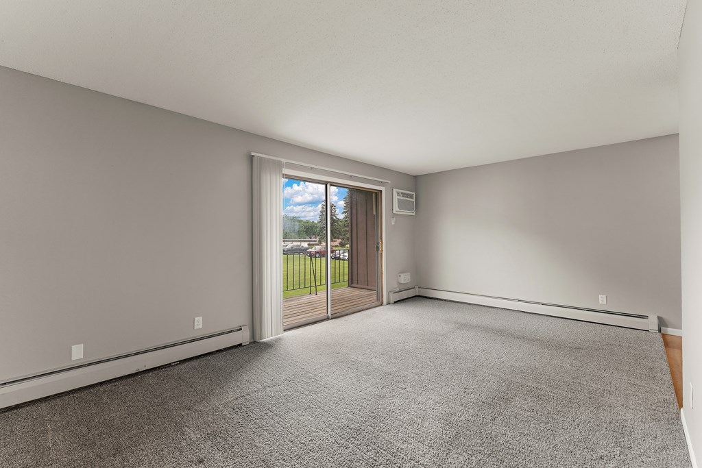 A room with a grey carpet and a sliding glass door leading to a balcony.