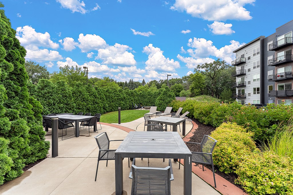 A patio with a table and chairs is surrounded by greenery.