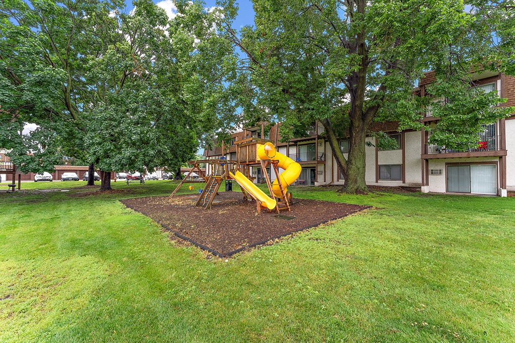 A playground with a yellow slide in the middle of a grassy area.