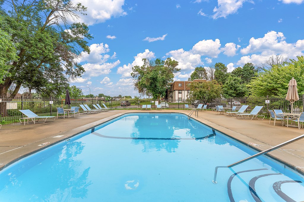 A large blue swimming pool surrounded by lounge chairs and trees.