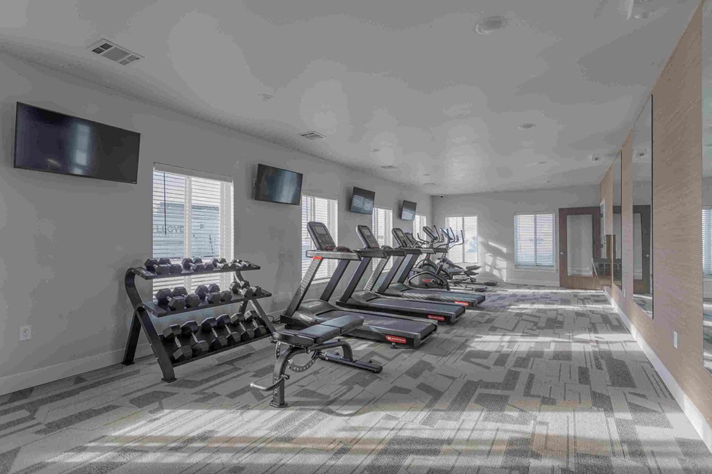 a row of cardio machines in a gym with a wall mounted tv
