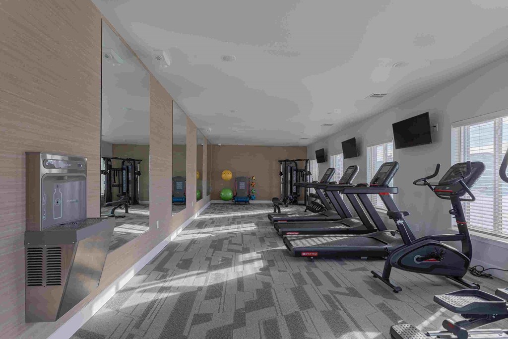 a gym with cardio equipment and a tv
