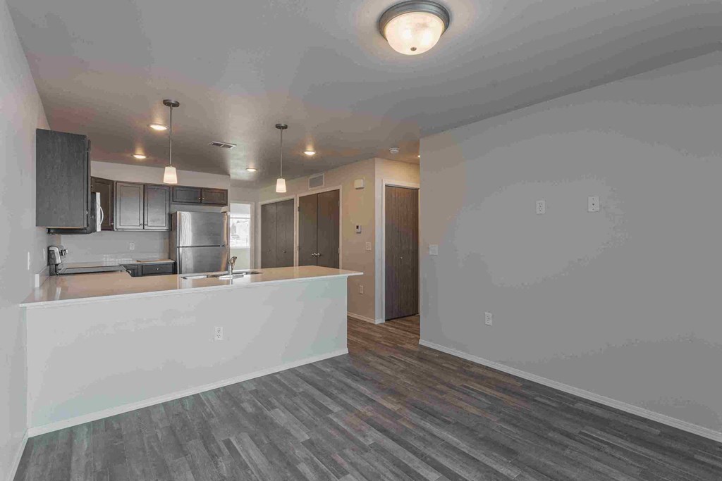 an empty living room and kitchen with a counter top and a refrigerator