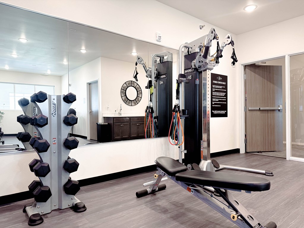 A gym with a variety of equipment including a leg press machine, dumbbells, and a bench.
