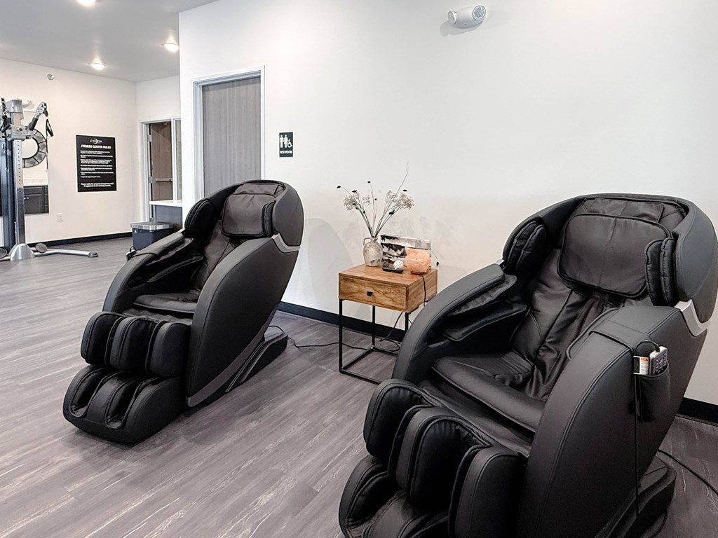 Two black massage chairs in a room with a wooden table and a vase of flowers.