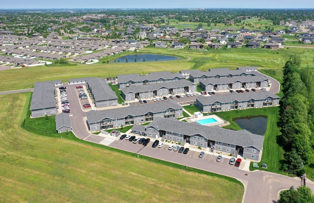 an aerial view of a group of houses near a field and a pond