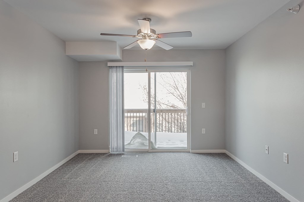 an empty living room with a ceiling fan and a sliding glass door