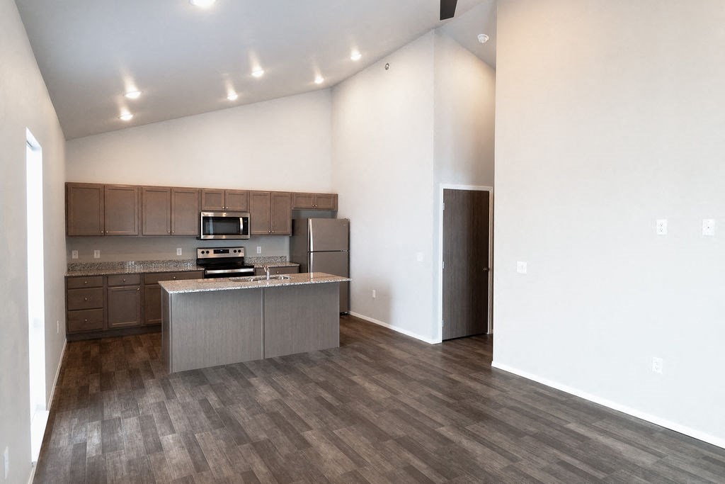 an empty living room with a kitchen with stainless steel appliances