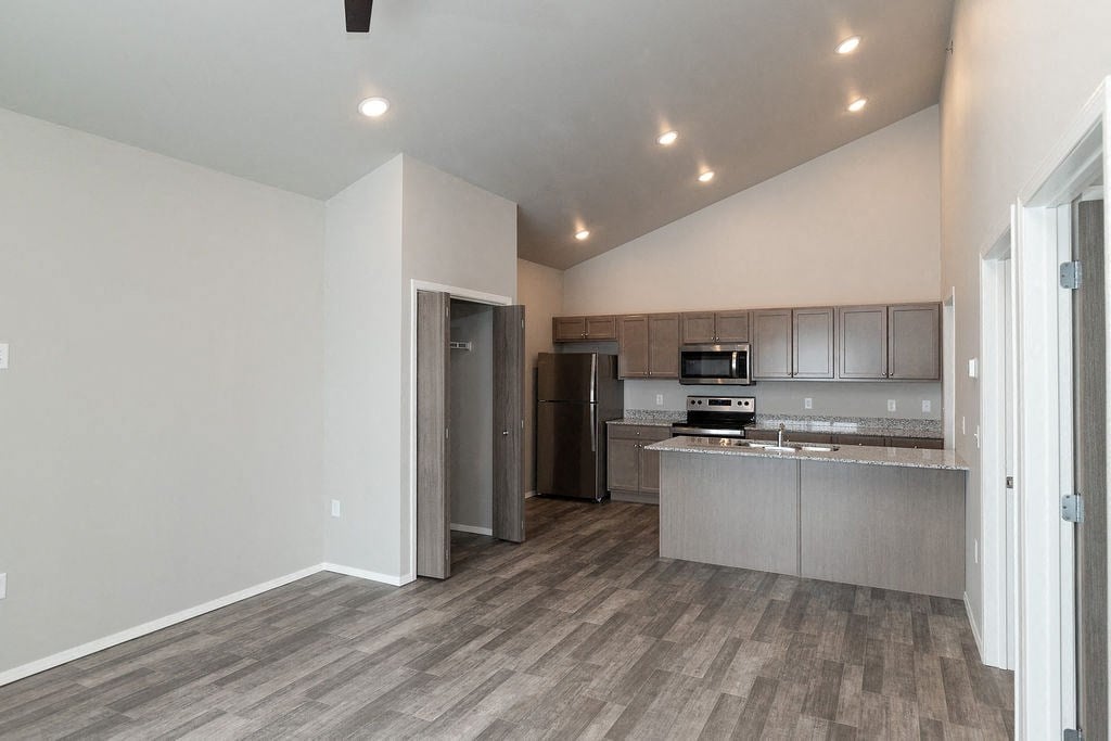 an empty living room with a kitchen with stainless steel appliances
