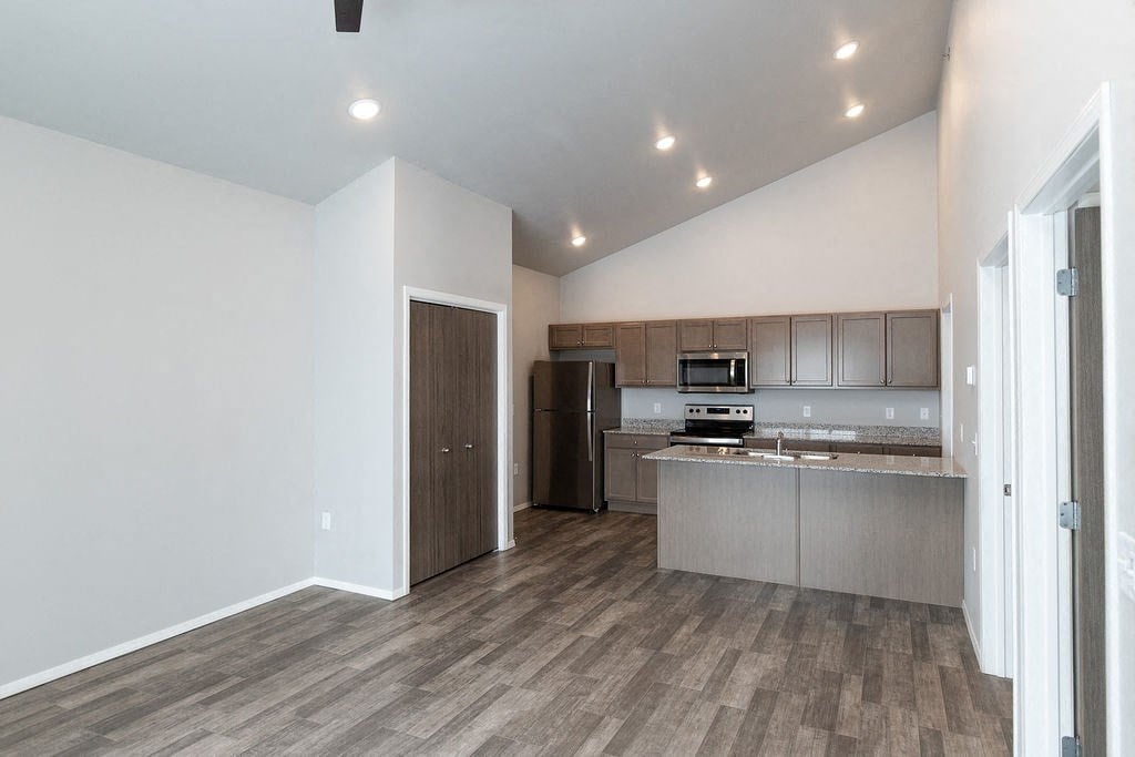 an empty living room with a kitchen with stainless steel appliances