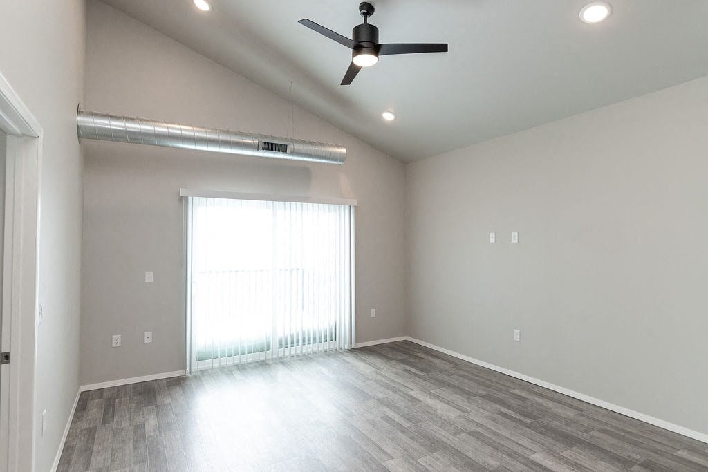 an empty living room with a large window and a ceiling fan