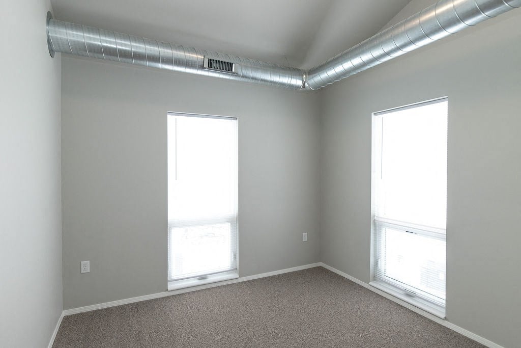 an empty room with two windows and a carpet