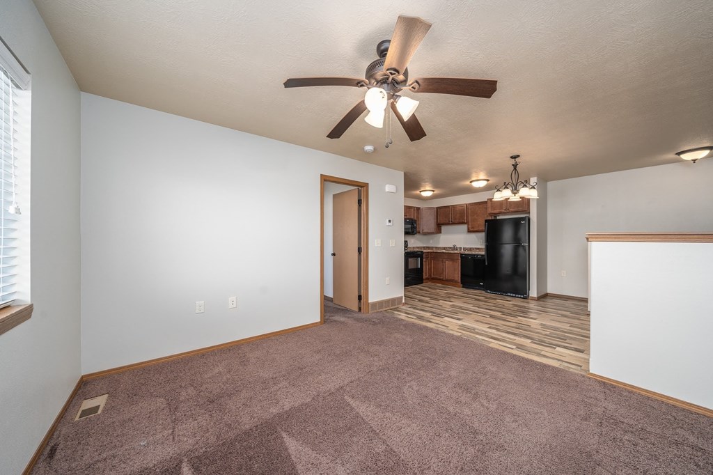 an empty living room with a ceiling fan and a kitchen
