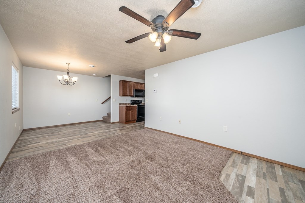 an empty living room with a ceiling fan and a kitchen