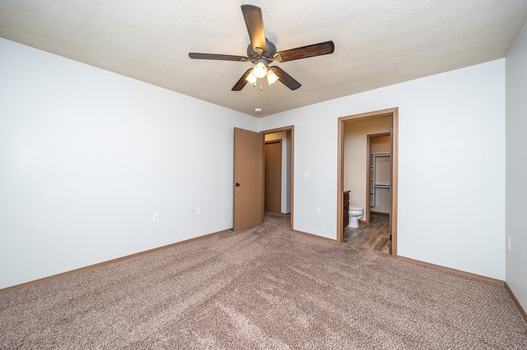 an empty living room with a ceiling fan and white walls