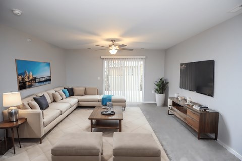 A living room with a large couch, a coffee table, and a flat-screen TV mounted on the wall.