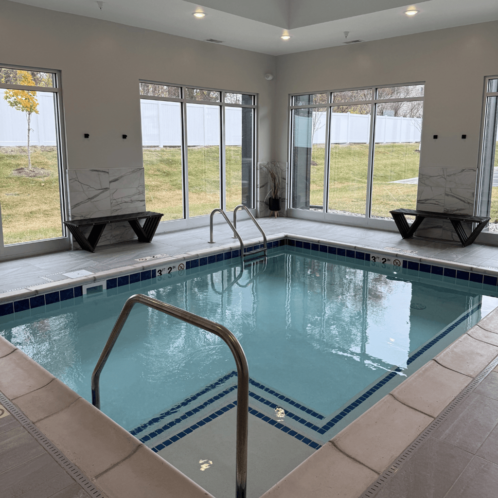 A large indoor swimming pool with a glass wall and a metal ladder.