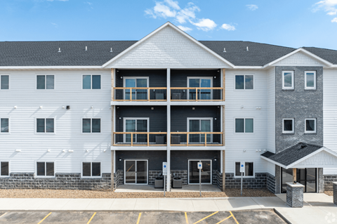 A white building with a black roof and a parking lot in front.