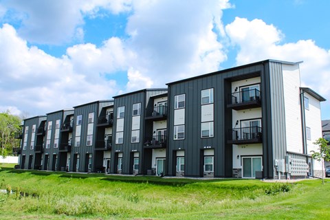A modern apartment building with balconies and a grassy area in front.