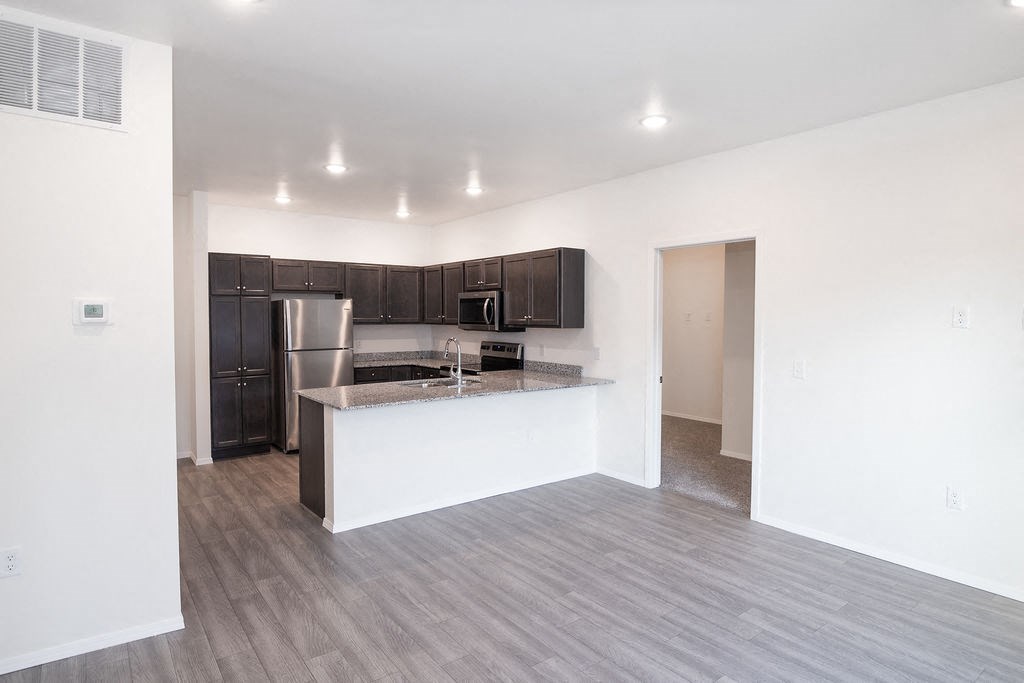 an empty living room with a kitchen with a counter and refrigerator