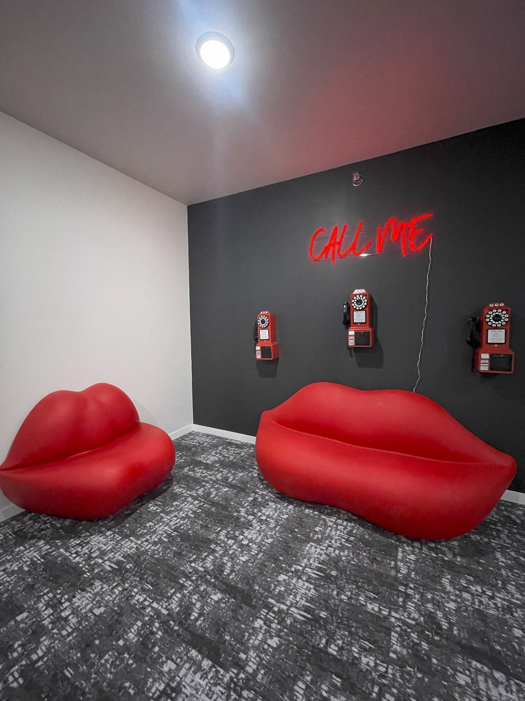 A room with a neon sign that says "call me" and two red couches.