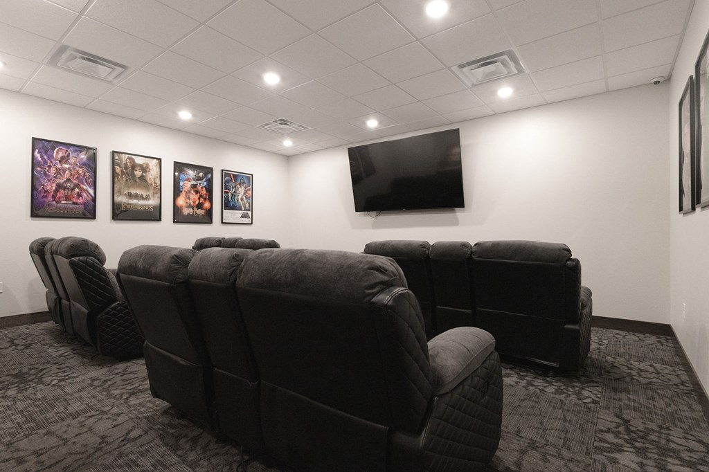 a room with a large screen television and a row of black leather chairs