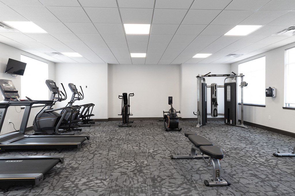 a gym with cardio equipment and weights in a room with windows
