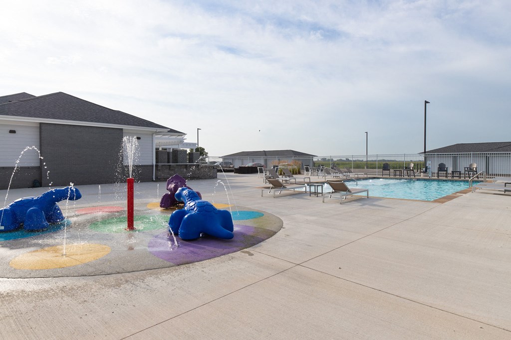 a swimming pool with two childrens fountains and lounge chairs in front of a building