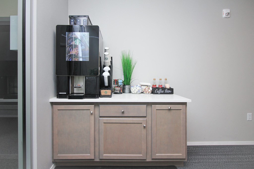 A black coffee maker on a wooden cabinet with a glass door.