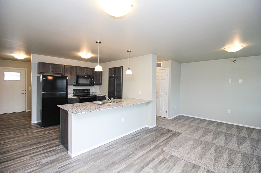 A kitchen with a black fridge and microwave, a white island, and a wooden floor.