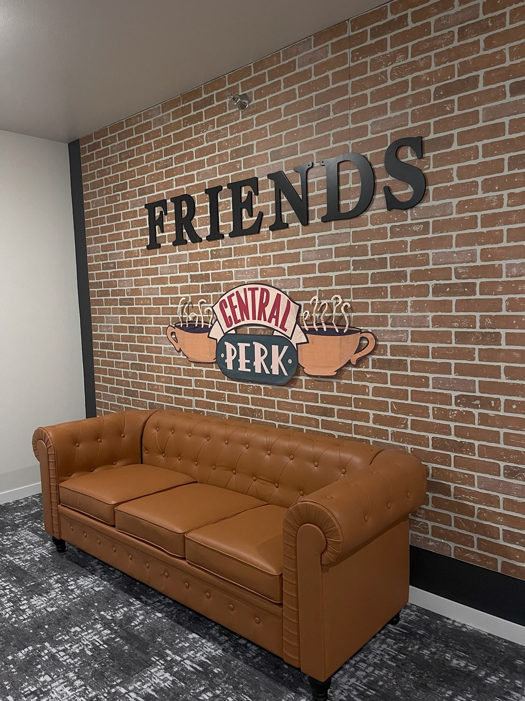 A brown couch sits in front of a brick wall with a Friends sign on it.