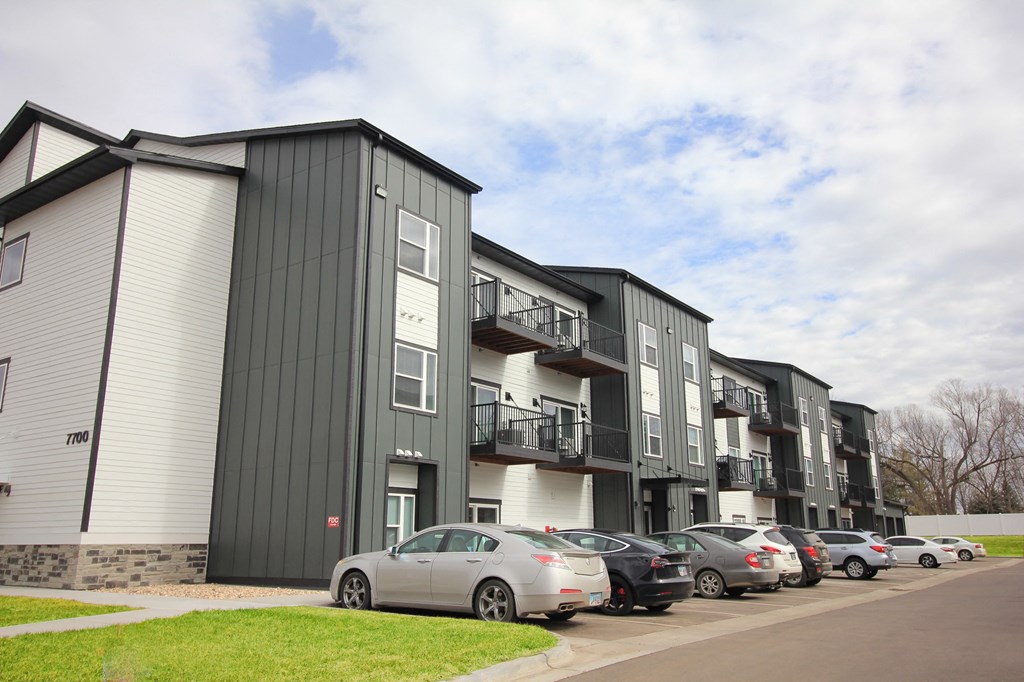 A car is parked in front of a building with a balcony.