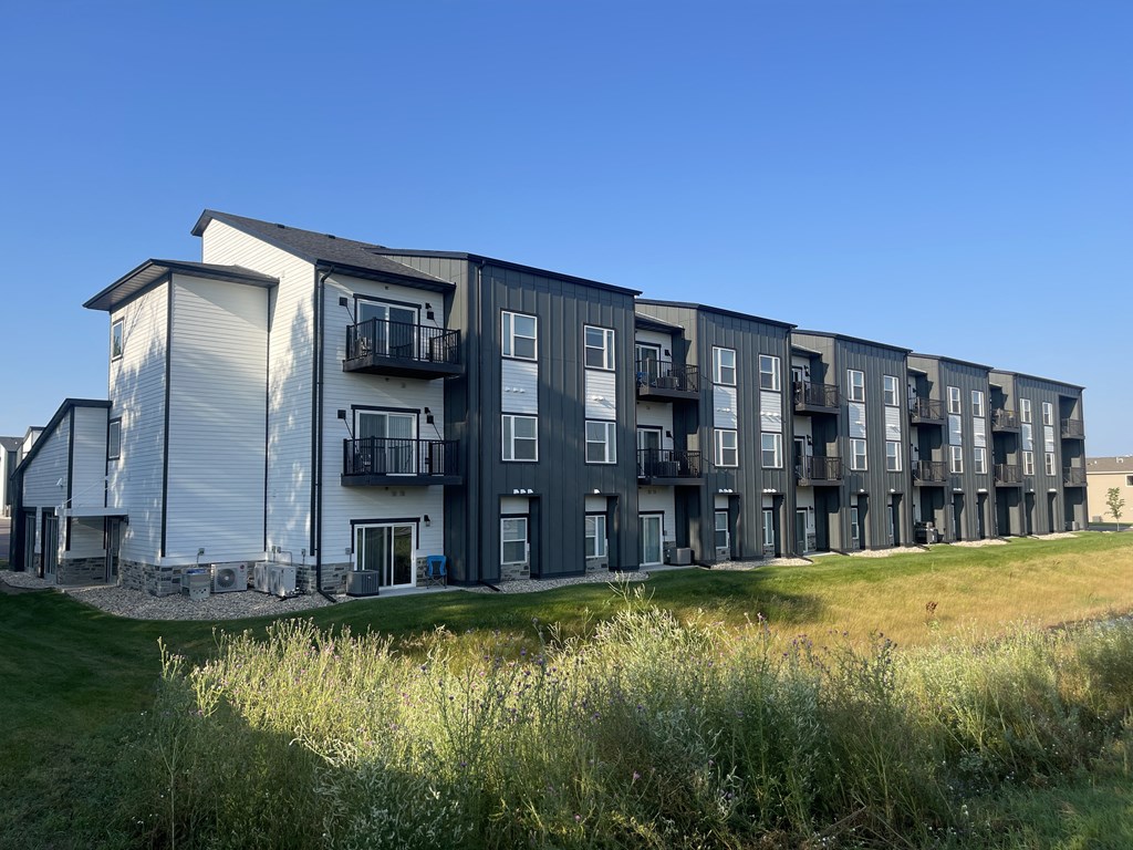 A row of modern townhouses with balconies and a grassy area in front.