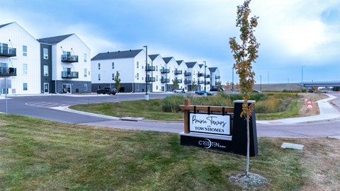 A sign for a development called "Pine Ridge Townhomes" is in front of a grassy area with apartment buildings in the background.