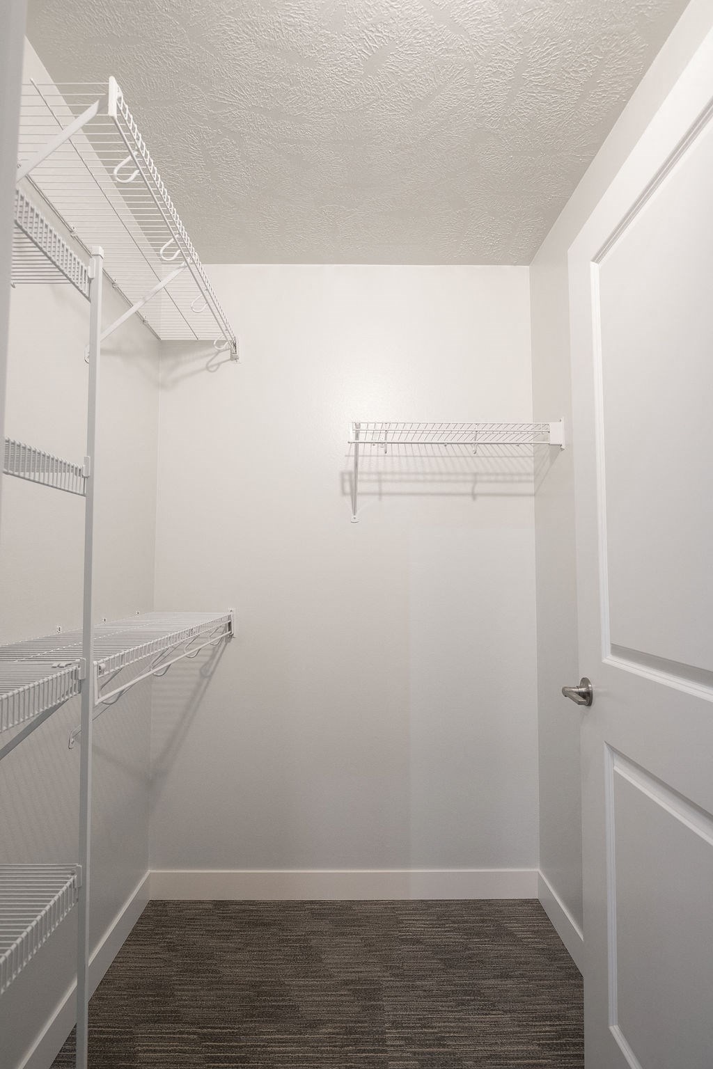 a walk in closet in a white room with shelves and a door