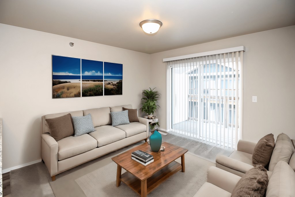 A living room with a couch, a coffee table, and a large window with a view of the outside.