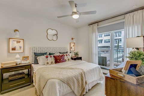 A bedroom with a large bed, a ceiling fan, and a window with a view of a balcony.