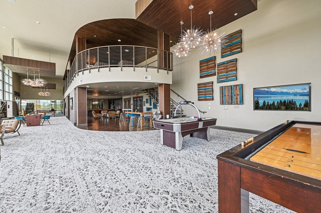 A billiard table is in the foreground of a spacious room with a staircase and a balcony.