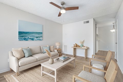 A living room with a beige couch, a coffee table, and a painting of a beach scene on the wall.