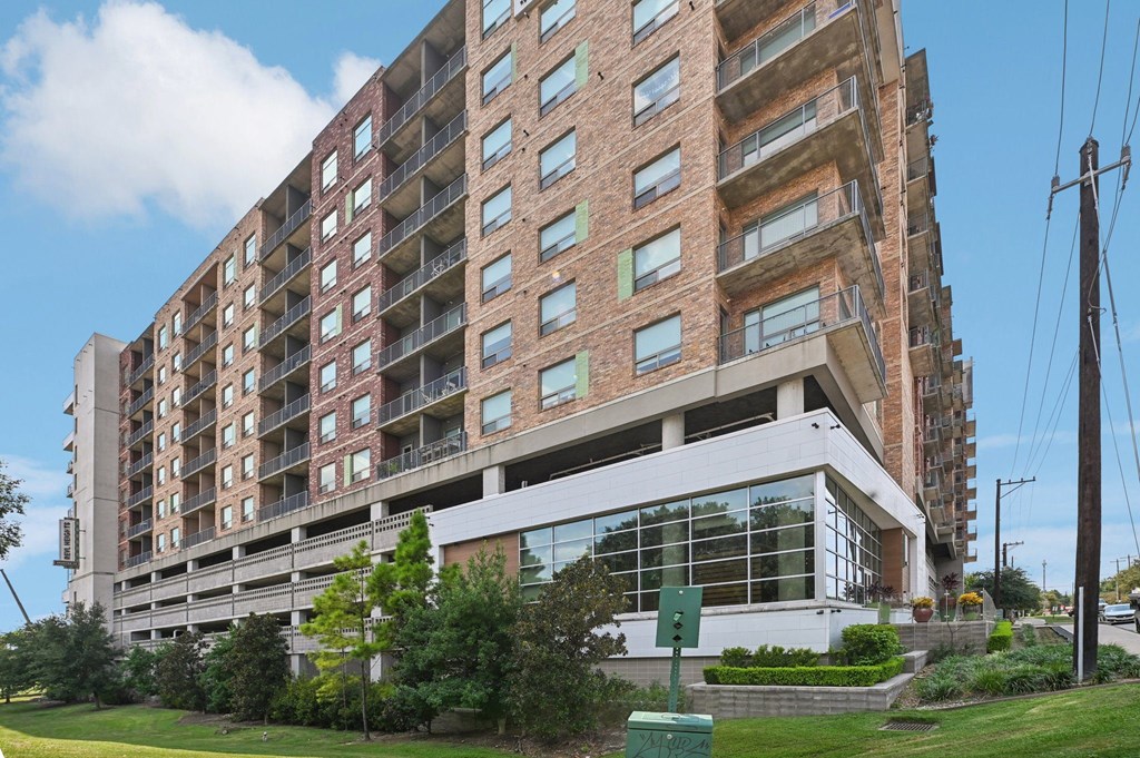 A large brick building with a white base and a green trash can in front.
