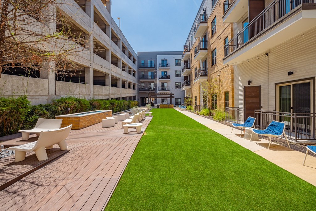 A sunny day at a modern apartment complex with a long wooden deck and lounge chairs.