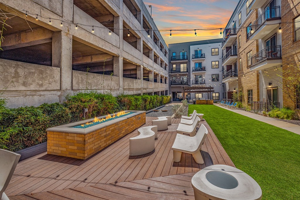 A wooden deck with benches and a hot tub is surrounded by buildings.